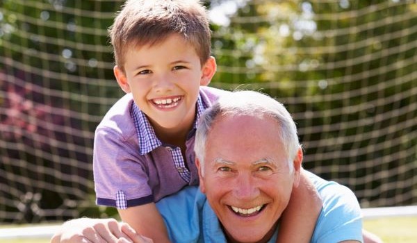 Particolare locandina: un nipote portato in spalla dal nonno su sfondo con rete di calcio.